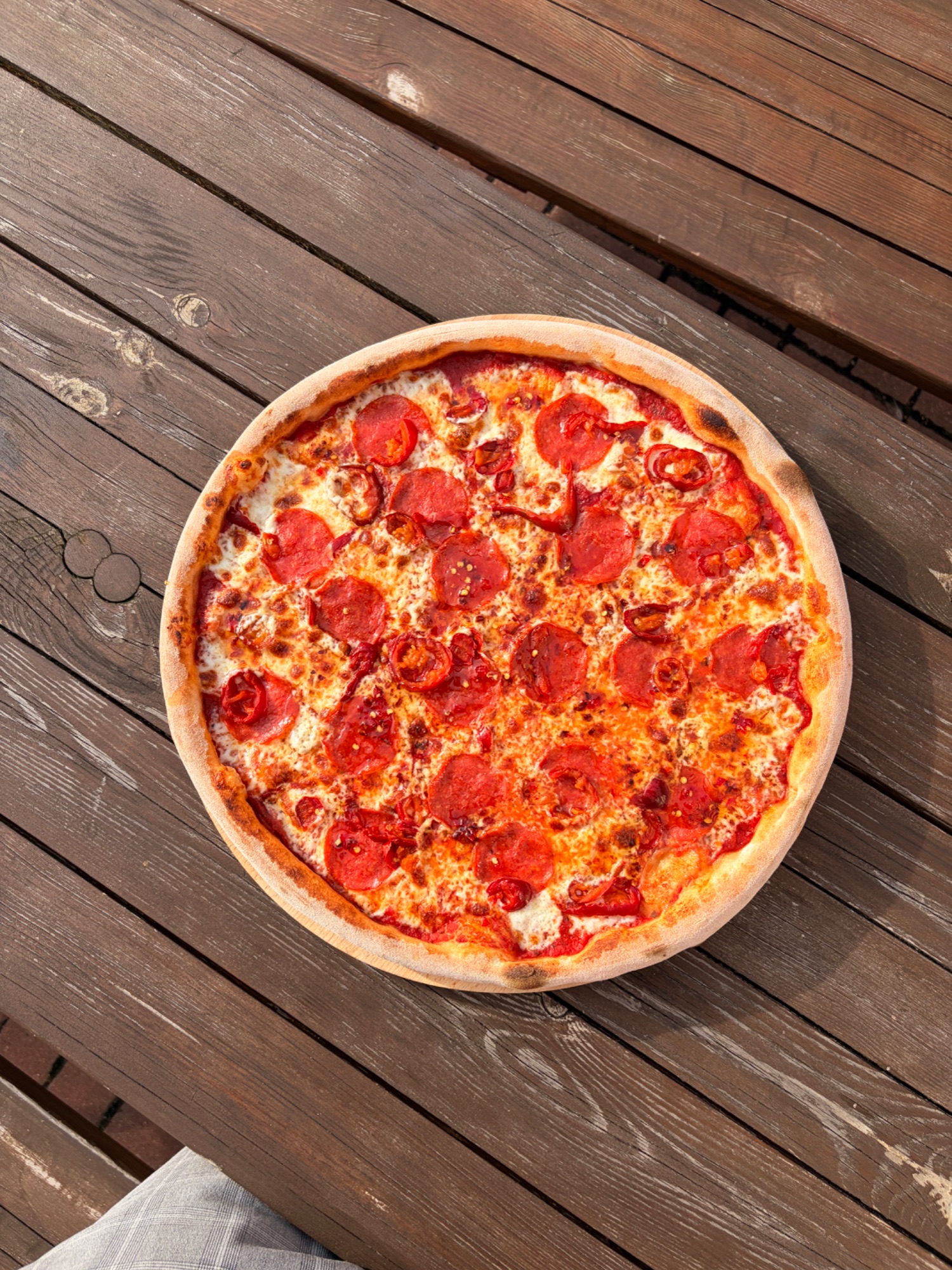 Pizza pepperoni na drewnianym stole, z chrupiącym ciastem i soczystymi plasterkami kiełbasy.