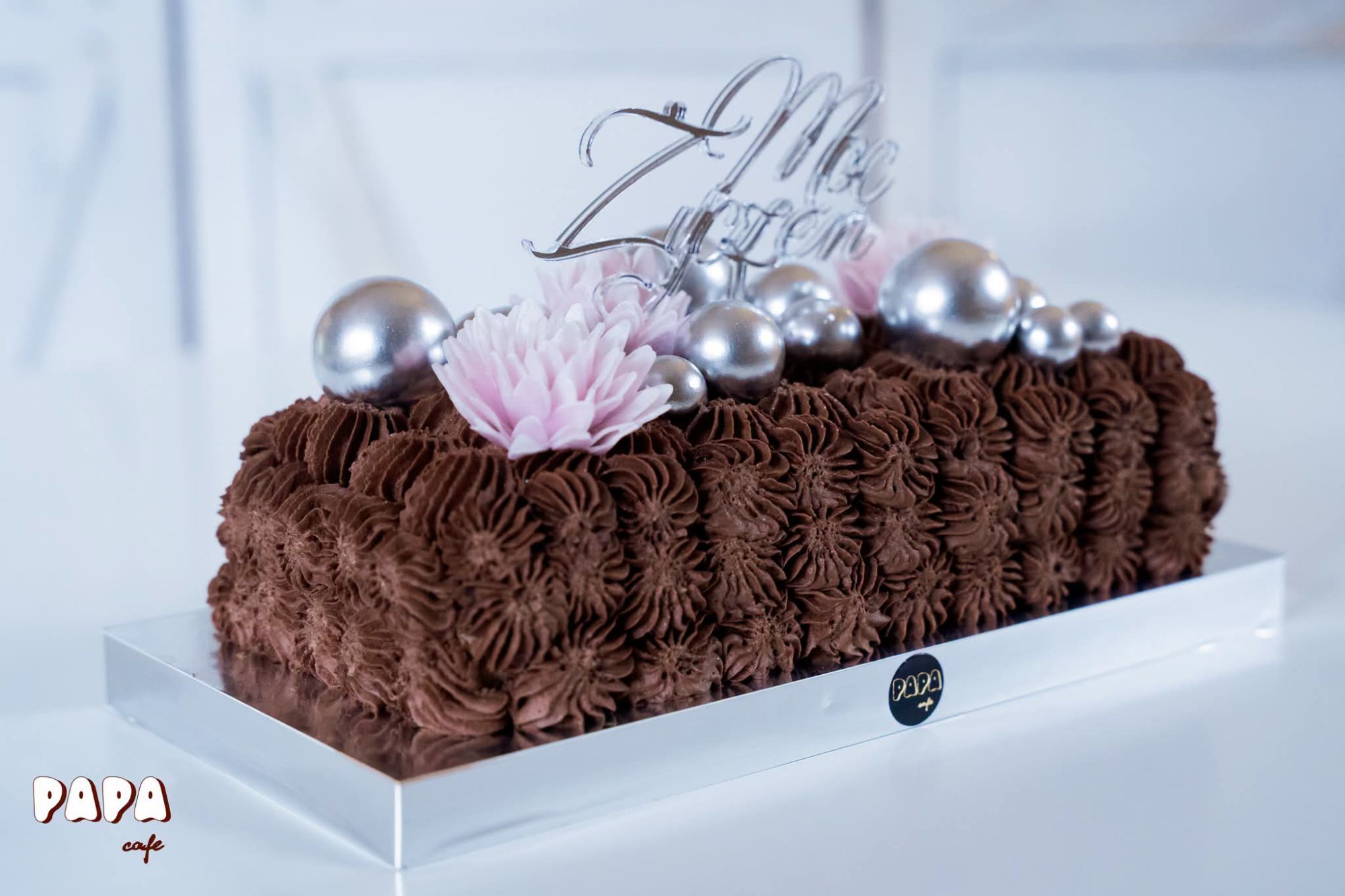 Elegancki tort czekoladowy ozdobiony perłami i kwiatami, z napisem "Mle Zyżon" na górze.