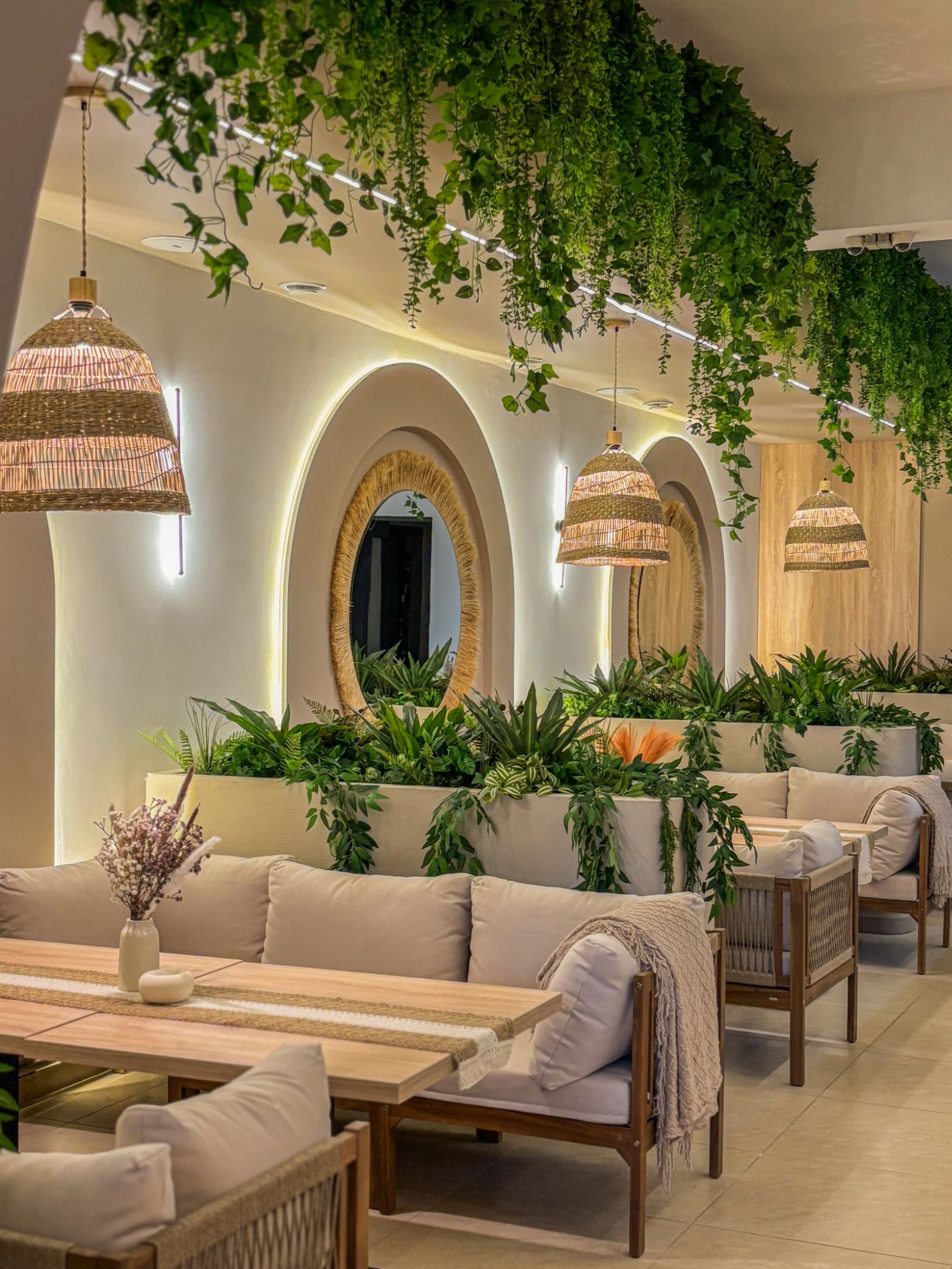 Stylowe wnętrze restauracji z roślinami, plecionymi lampami i przytulnymi sofami, oświetlone miękkim światłem.