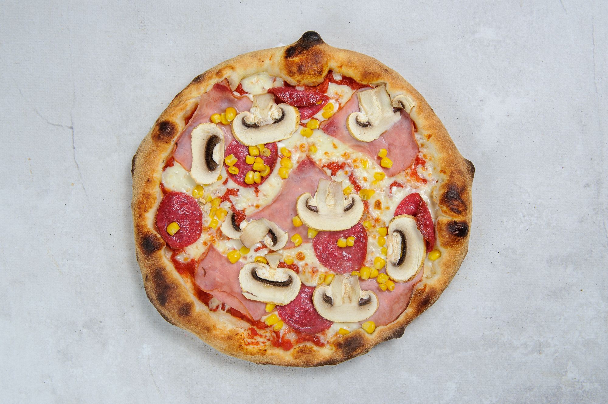 Pizza z serami, szynką, pieczarkami i kukurydzą na wypieczonym cieście.