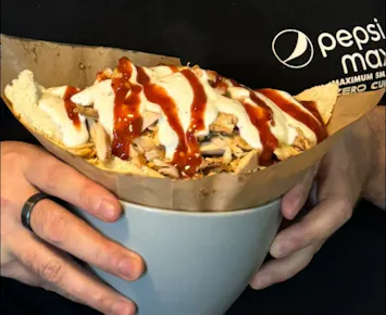 Osoba trzymająca miskę z daniem kebabowym, przykrytym sosem jogurtowym i sosem pomidorowym.