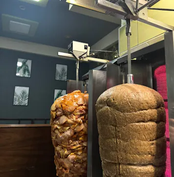 Obrót pieczonego mięsa i chleba w lokalu gastronomicznym, z dekoracyjnymi roślinami w tle.
