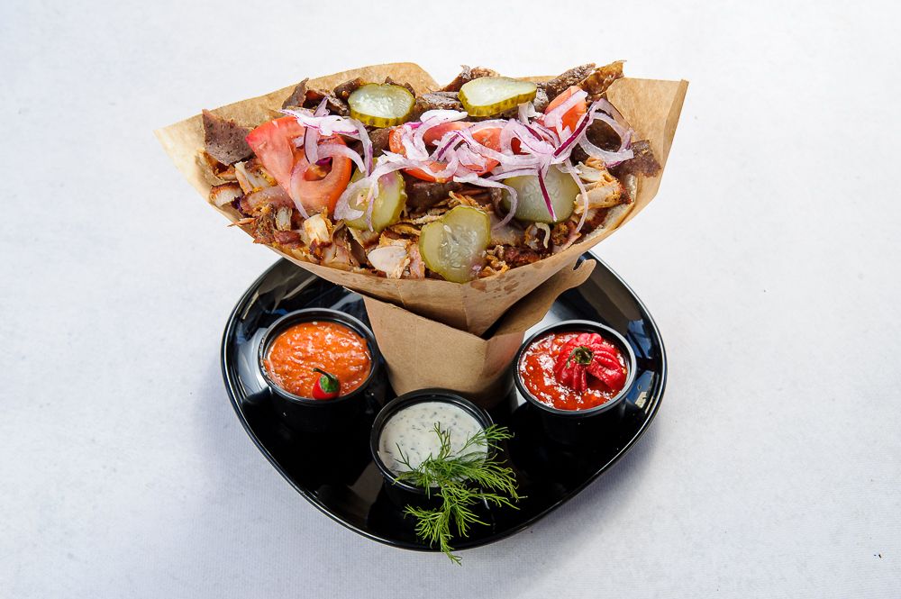 Kebab w papierze z mięsem, warzywami i sosami na czarnym talerzu, ozdobiony świeżymi ziołami.