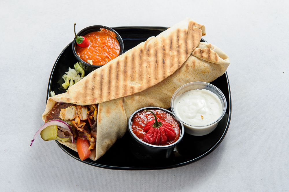 Tortilla z mięsem, warzywami i sosami w czarnym talerzu.