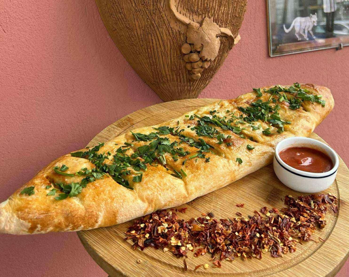 Chlebek turecki z ziołami, podany z sosem i przyprawami chili na drewnianym talerzu.