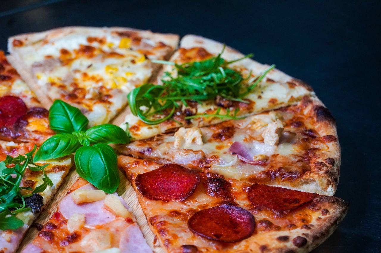 Pizza z różnymi dodatkami, w tym salami, kurczakiem, serem i świeżą bazylią, na ciemnym tle.