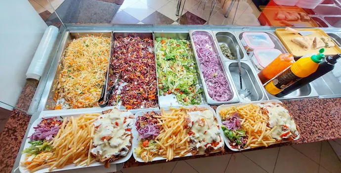 Stół bufetowy z frytkami, sałatkami i sosami, przygotowanymi w jasnych pojemnikach w restauracji fast food.