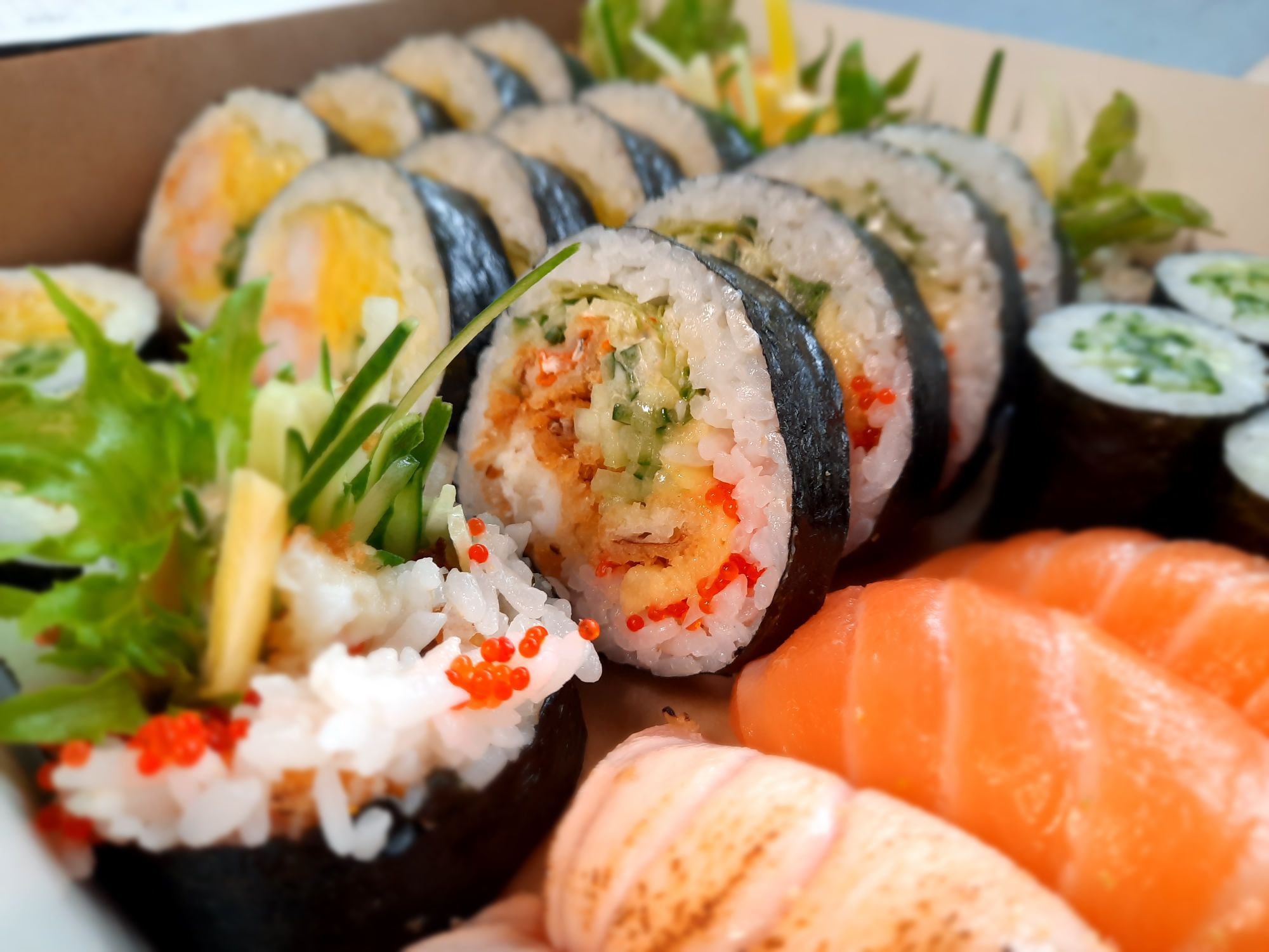 Sushi w pudełku, z różnorodnymi rolkami, surową rybą i świeżymi dodatkami.