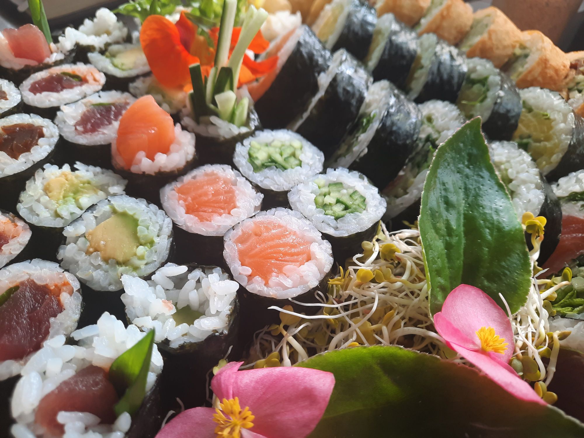 Różnorodne sushi z rybami, warzywami i ozdobami roślinnymi.