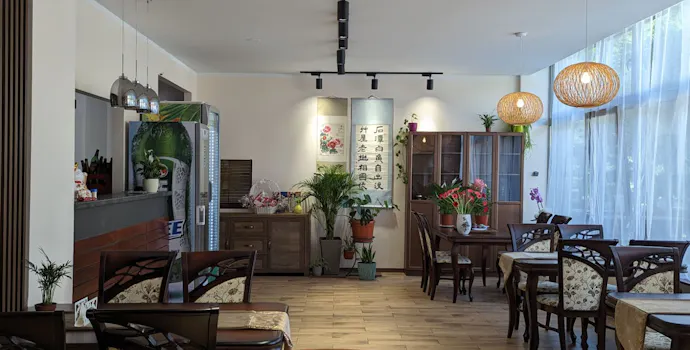 Nowoczesna restauracja z jasnym wnętrzem, drewnianymi meblami i roślinami w dekoracji.