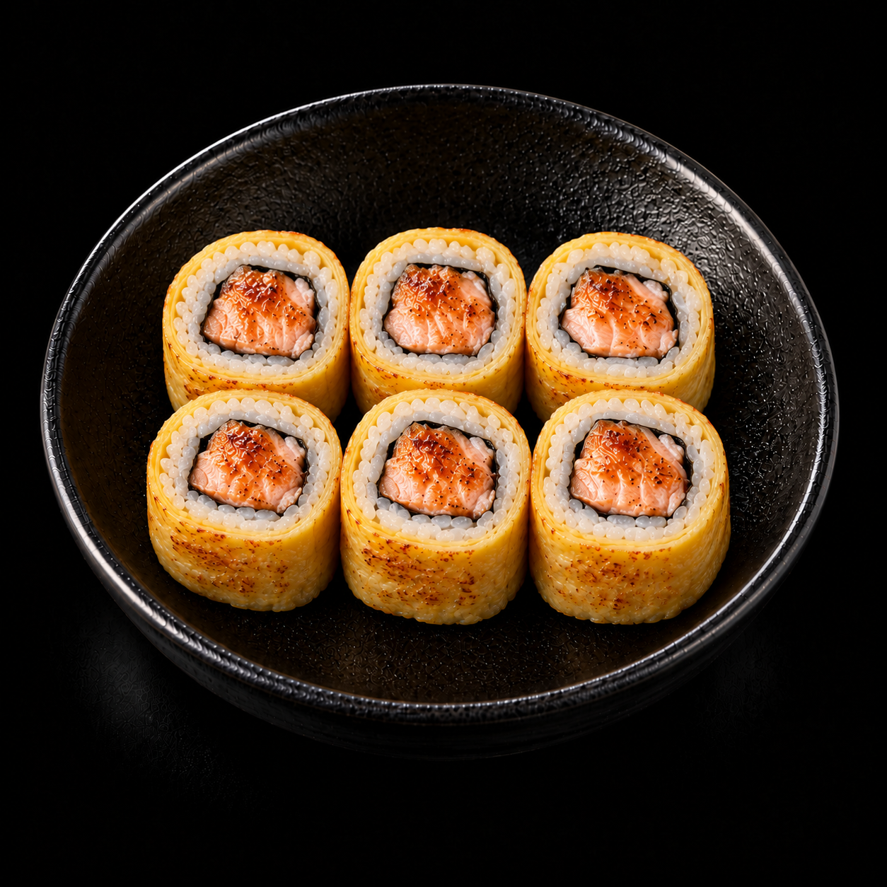 Sześć rolki sushi z grillowanym łososiem na czarnym talerzu.