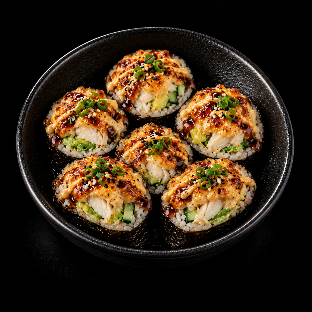 Sushi z kurczakiem i sosem, podane w czarnej misce, posypane zieloną cebulką.