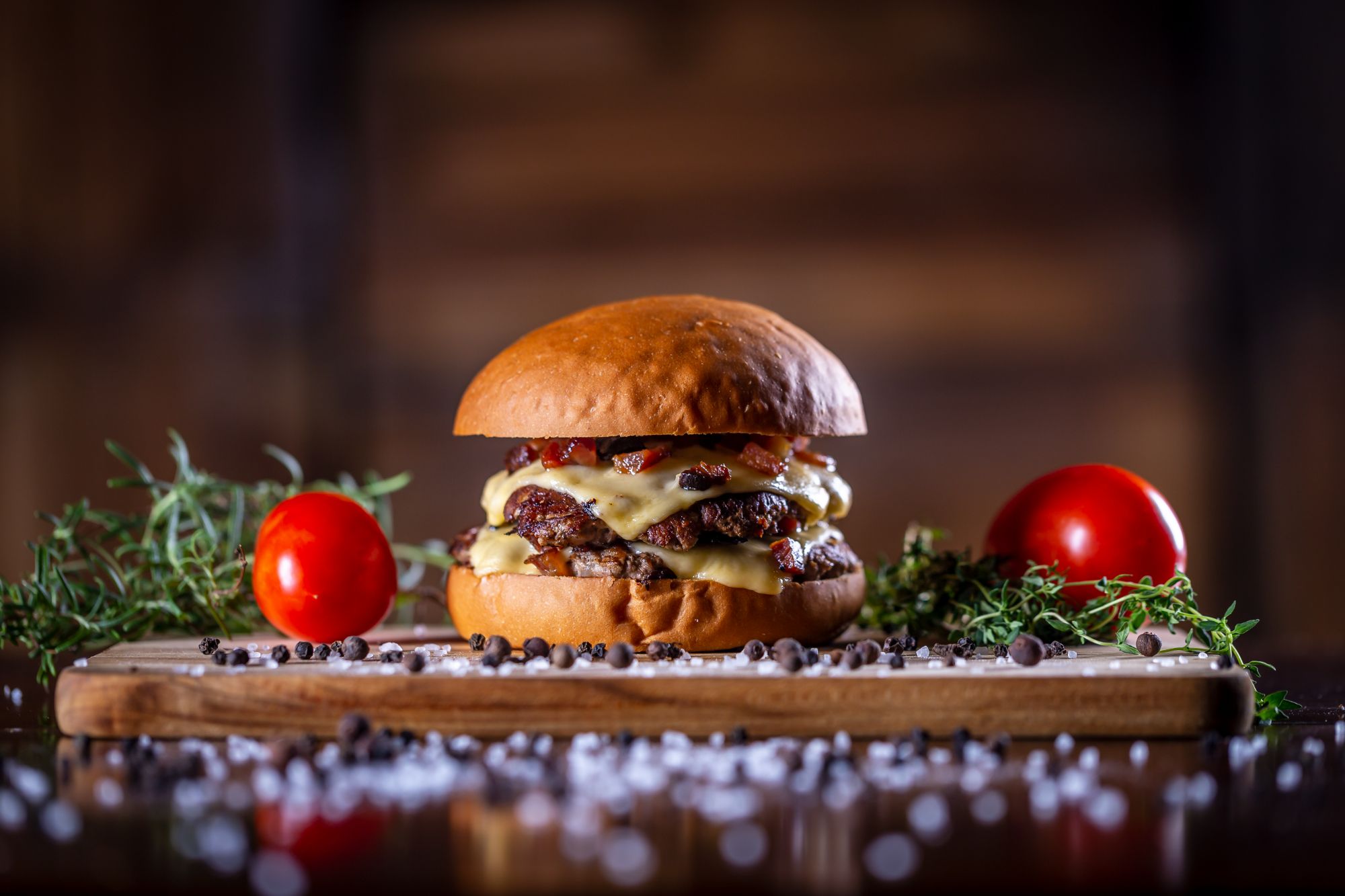 Šťavnatý hamburger s dvoma mäsovými plátkami, syrom, paradajkami a bylinkami na drevenej doske.