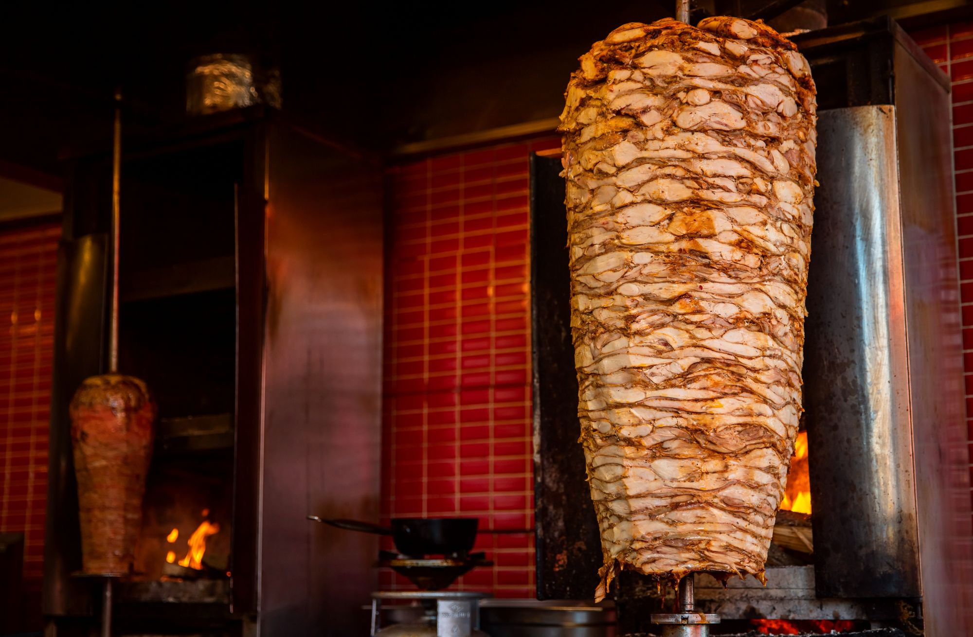 Otáčajúca sa shawarma na rožni v modernom prostredí kuchyne s červenou tehlovou stenou.