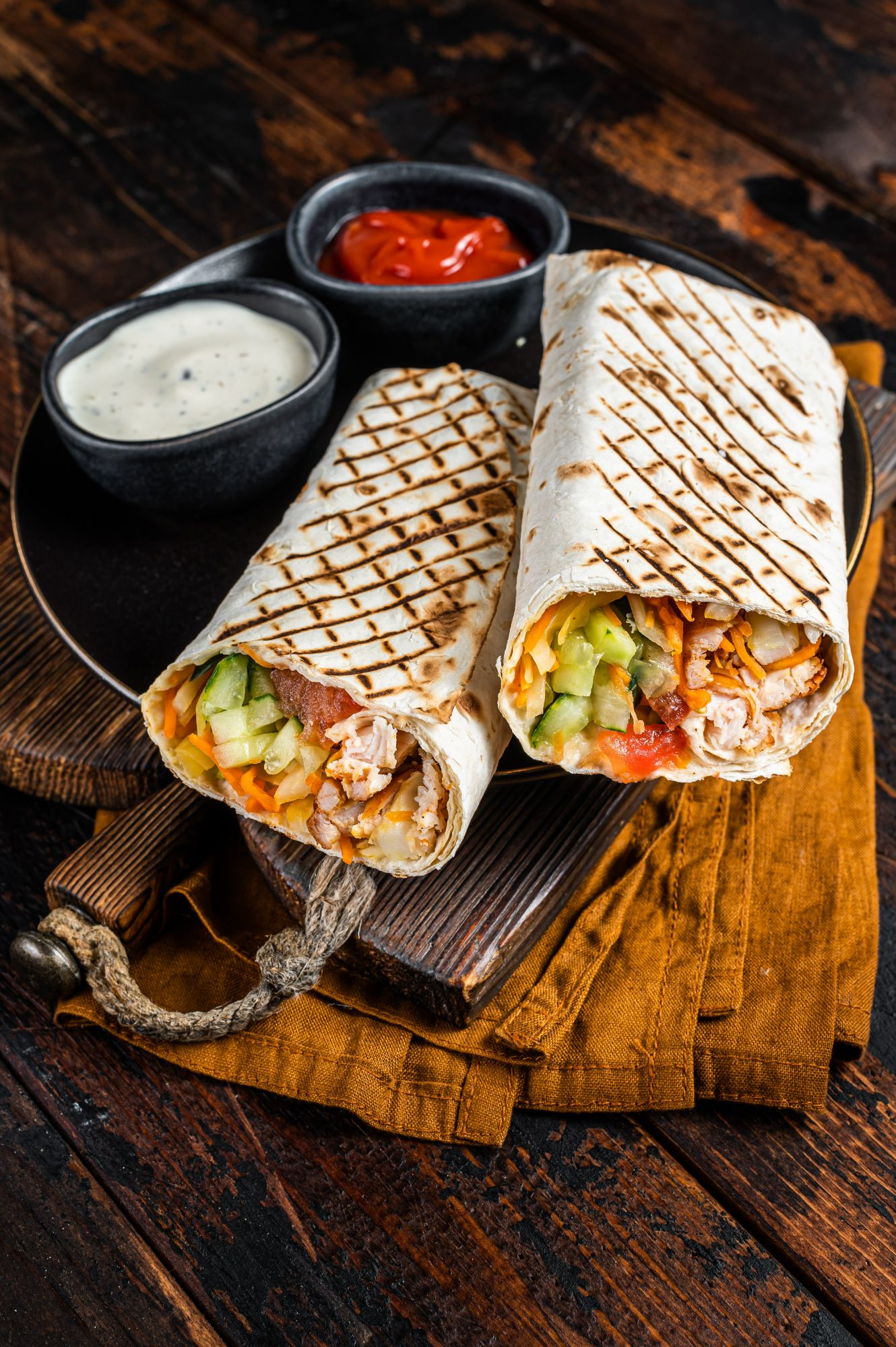 Grilované wrapy plnené kuracím mäsom, zeleninou a omáčkami na tanieriku.