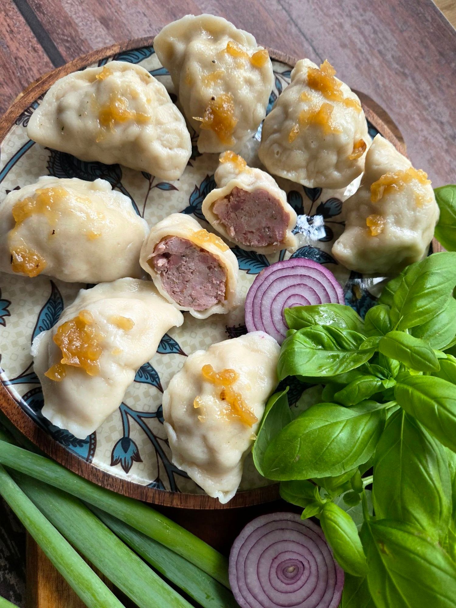 Pierogi z mięsem, podane na talerzu z cebulą, bazylią i zieloną cebulką.