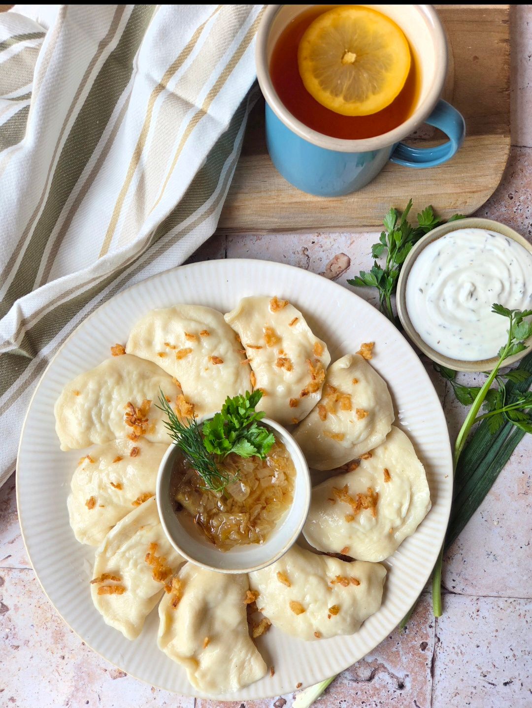 Pierogi z cebulą, podane z sosem, świeżą cebulką, koperkiem i herbatą z cytryną.