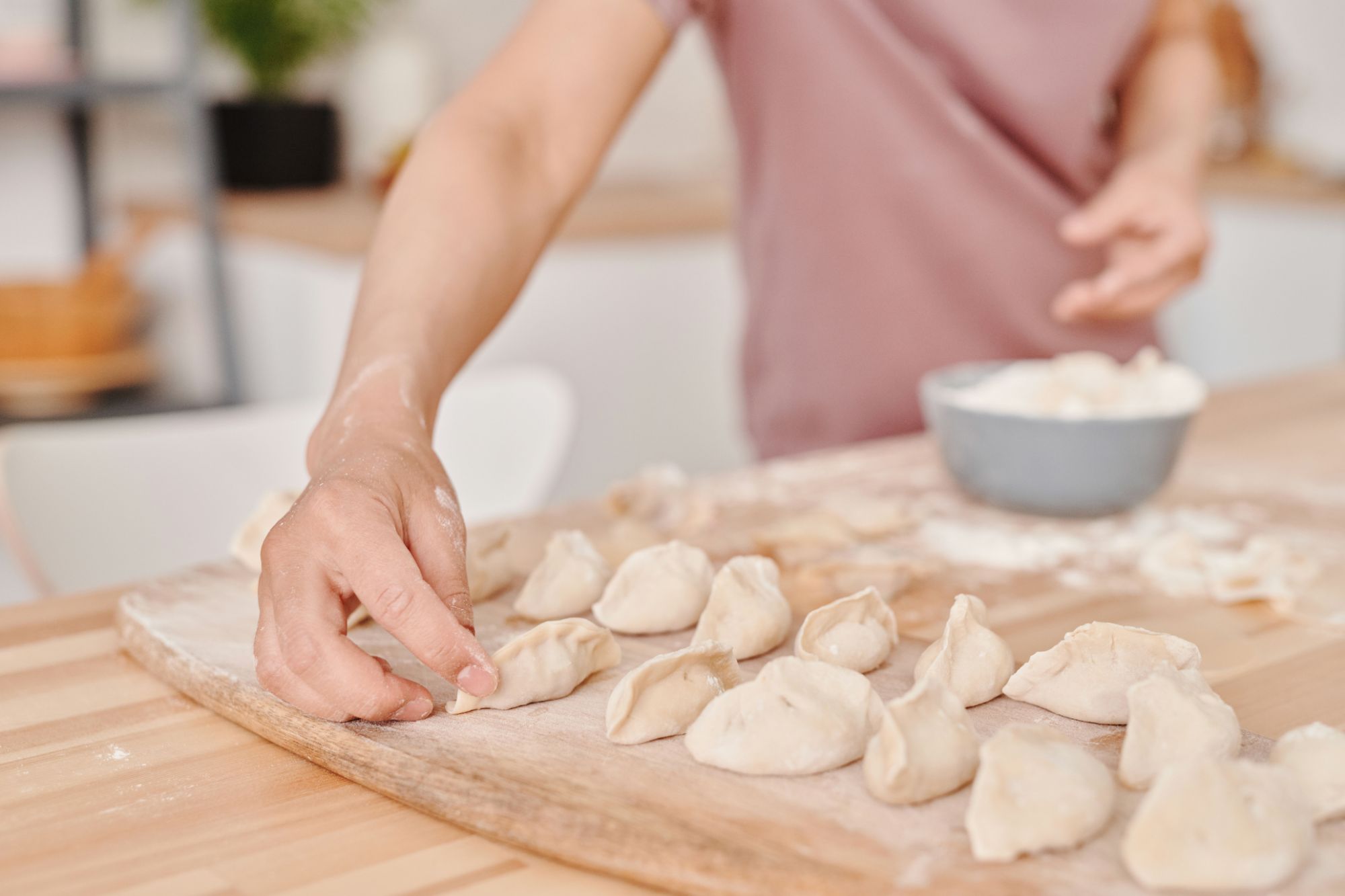 Osoba lepi pierogi na drewnianym blacie, obok stoi miska z nadzieniem.
