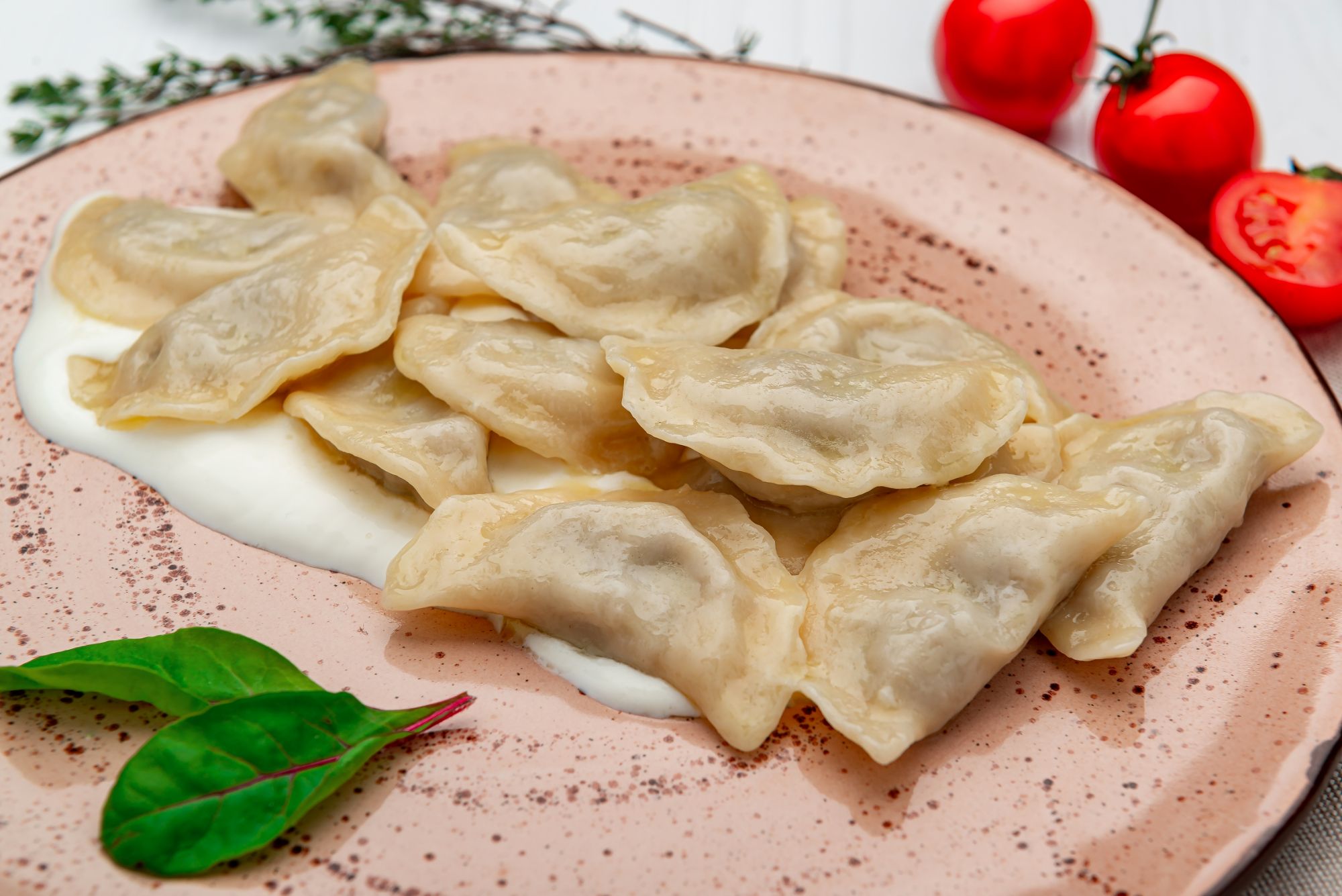 Pierogi na talerzu z sosem, obok pomidory i świeże zioła.