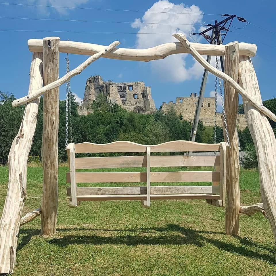 Huśtawka z drewna na tle ruin zamku pod błękitnym niebem i zielonymi drzewami.