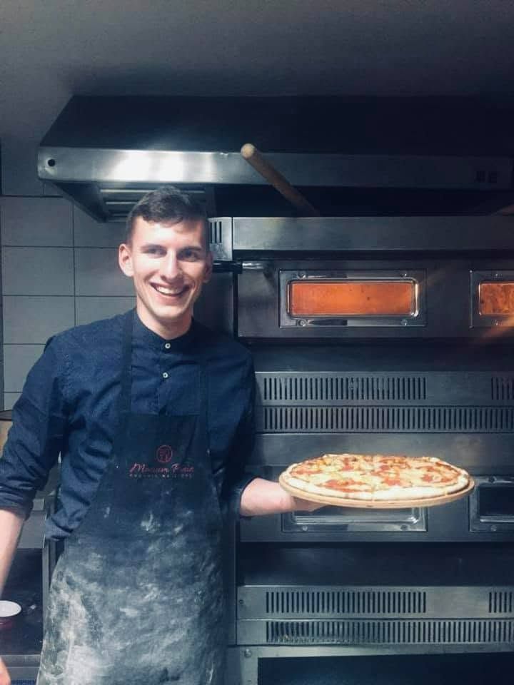 Mężczyzna w koszuli trzyma pizzę przed piecem w restauracji.