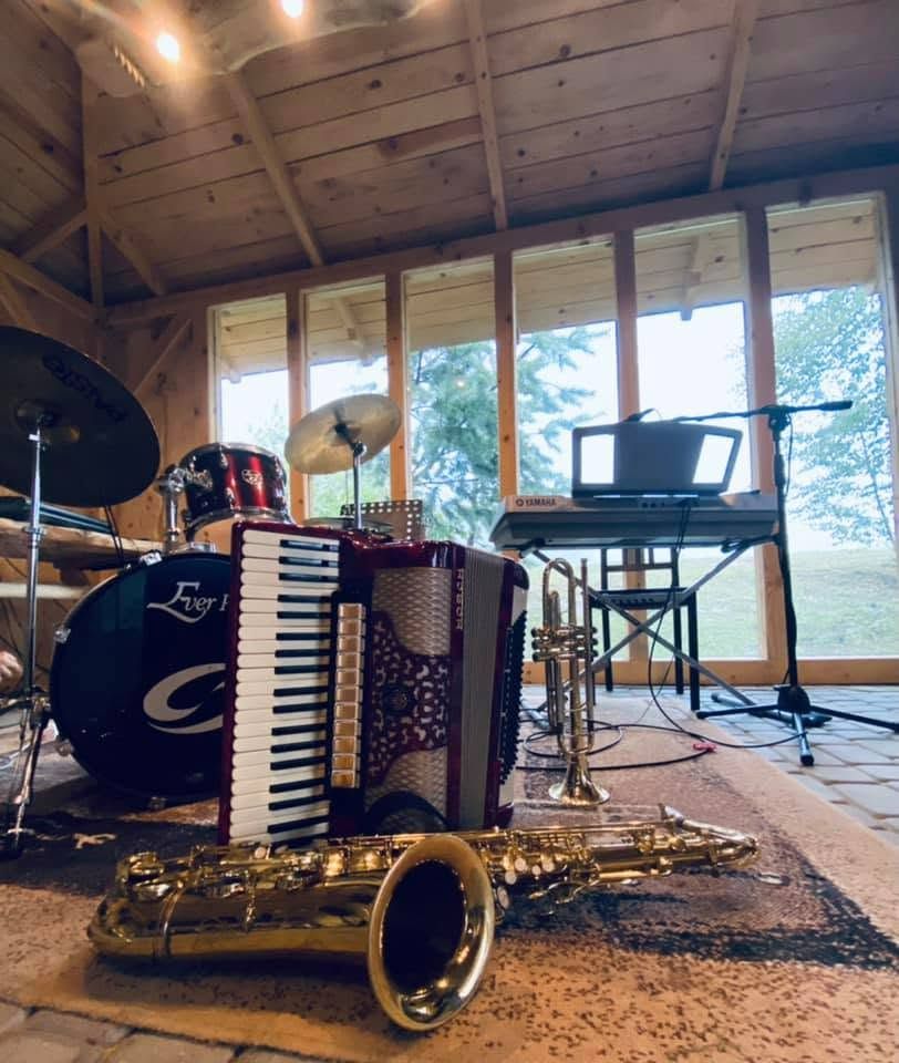Zestaw instrumentów muzycznych: akordeon, saksofon, trąbka, perkusja i keyboard w drewnianym pomieszczeniu.