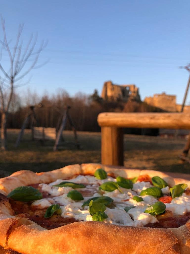 Pizza z sosem pomidorowym, serem i bazylią na tle ruin zamku w przyjemnej scenerii o zachodzie słońca.