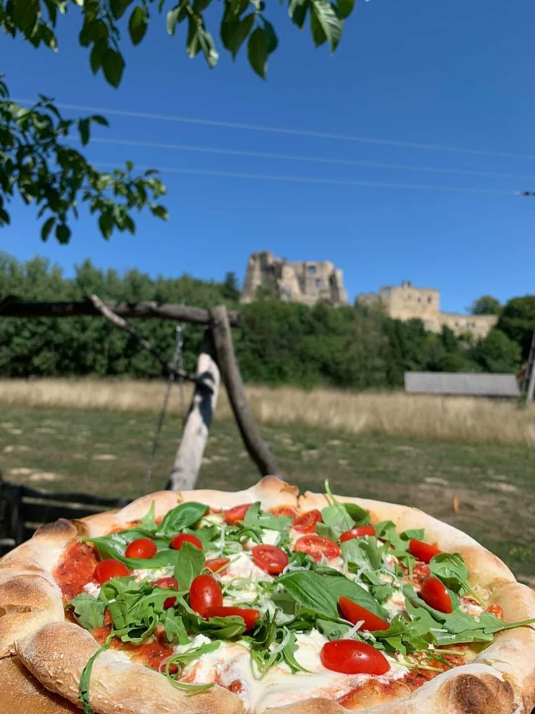 Pizza z rukolą i pomidorkami, z zamkiem w tle na tle nieba.