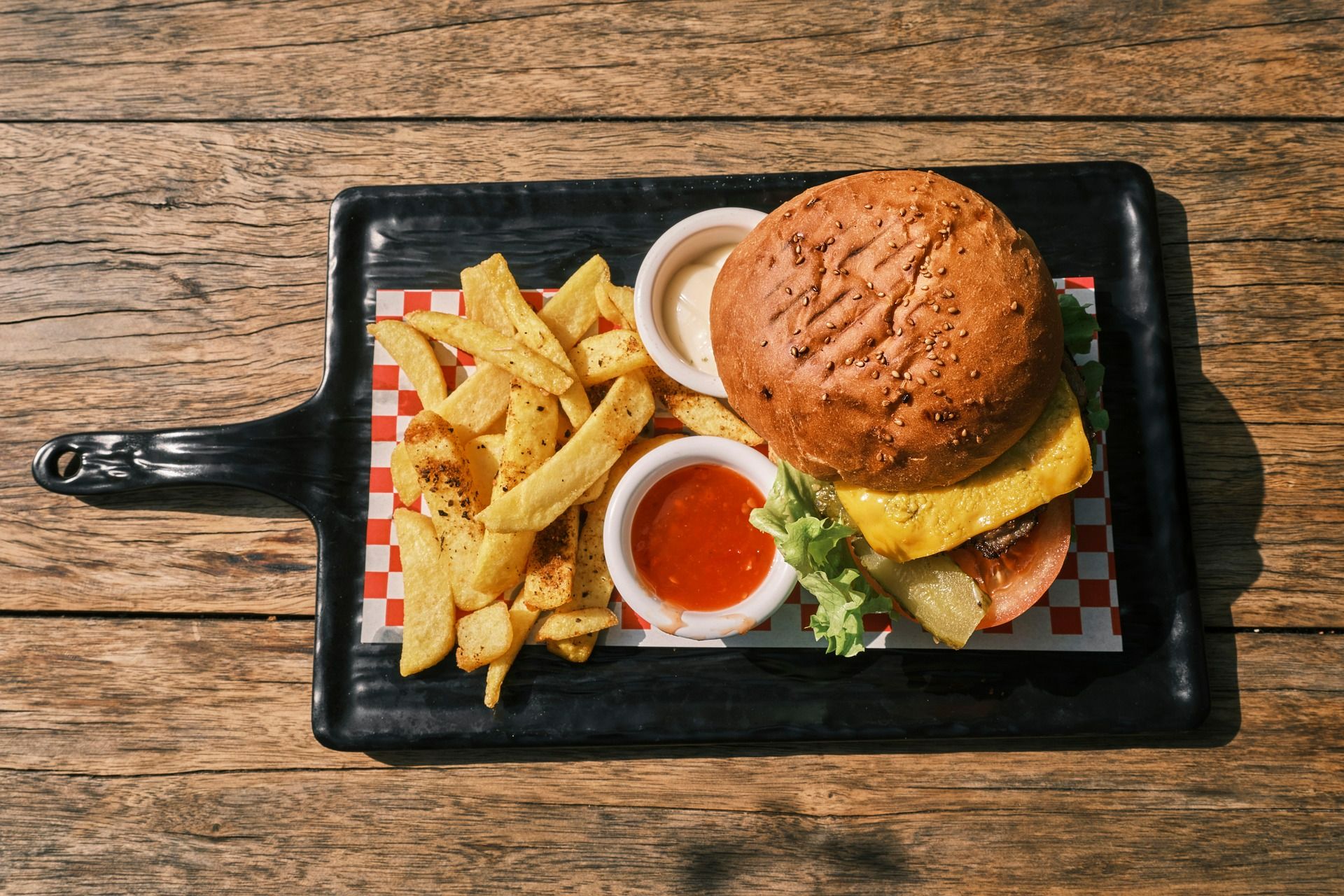 Burger z serem, sałatą i pomidorem, podany z frytkami i dwoma sosami na desce.