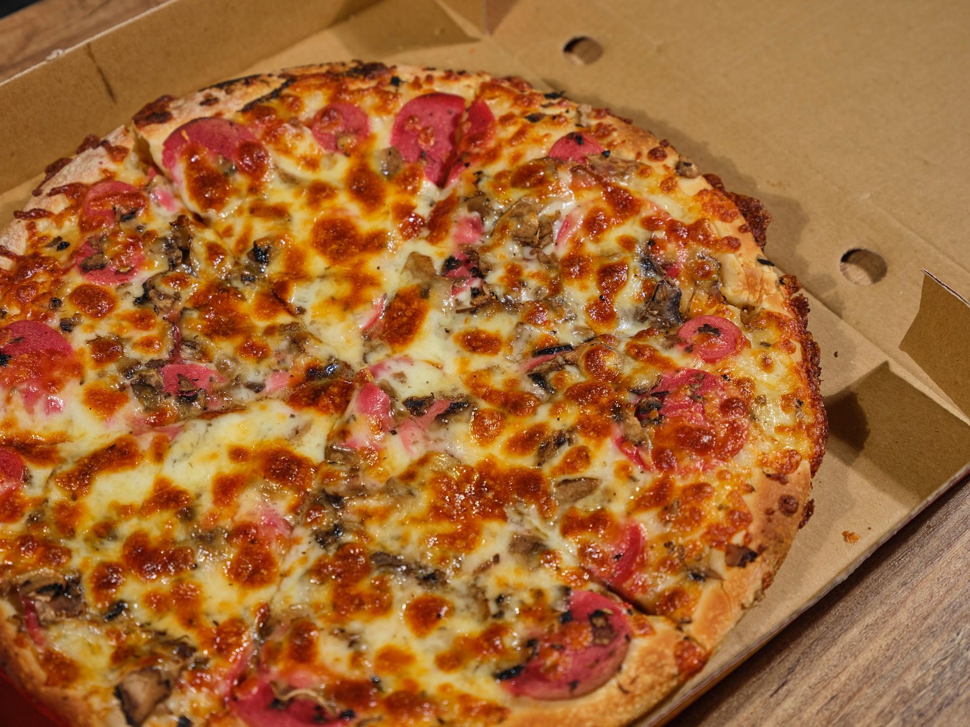 Pizza z pepperoni, pieczarkami i serem, podana w kartonowym opakowaniu.
