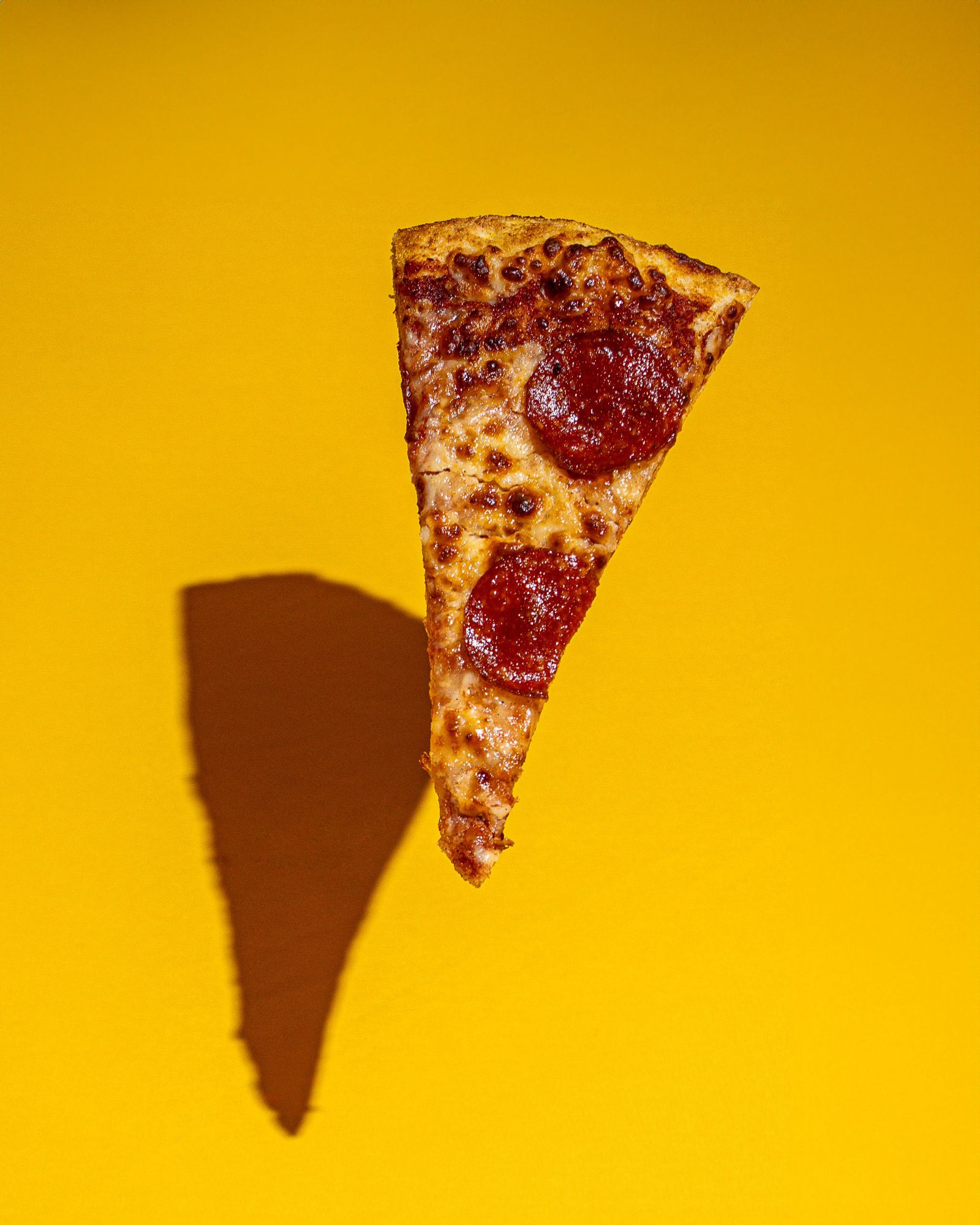 Kawałek pizzy pepperoni na żółtym tle, rzucający cień.