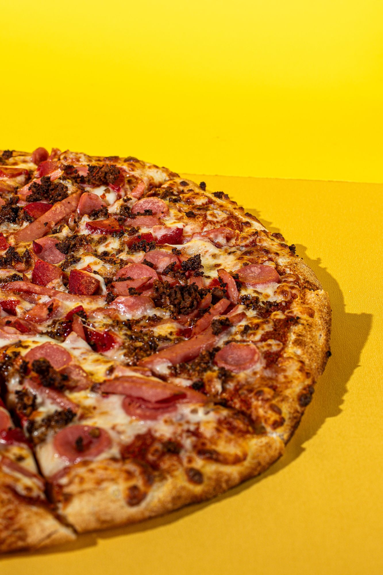 Pyszna pizza z serem, szynką i mięsem na tle żółtej tkaniny.
