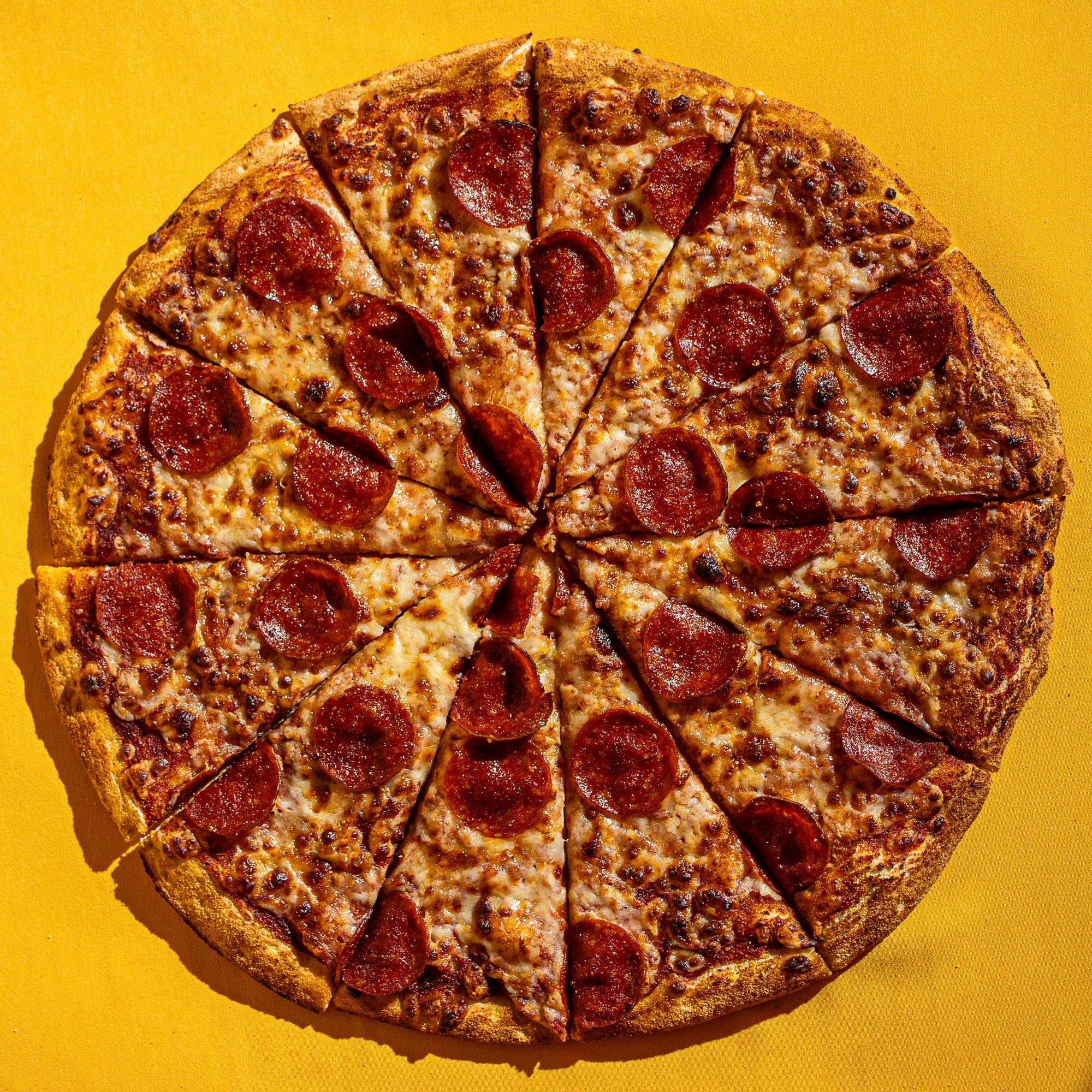 Pizza z pepperoni pokrojona w 16 kawałków na żółtym tle.
