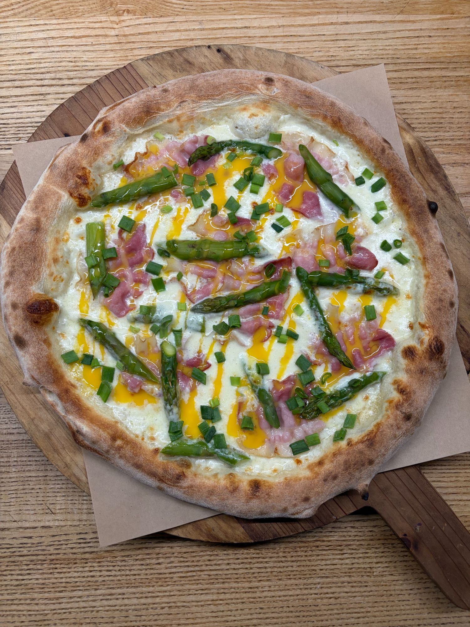 Pizza z zielonymi szparagami, szynką, serem cheddar i posypką z cebuli na drewnianej desce.