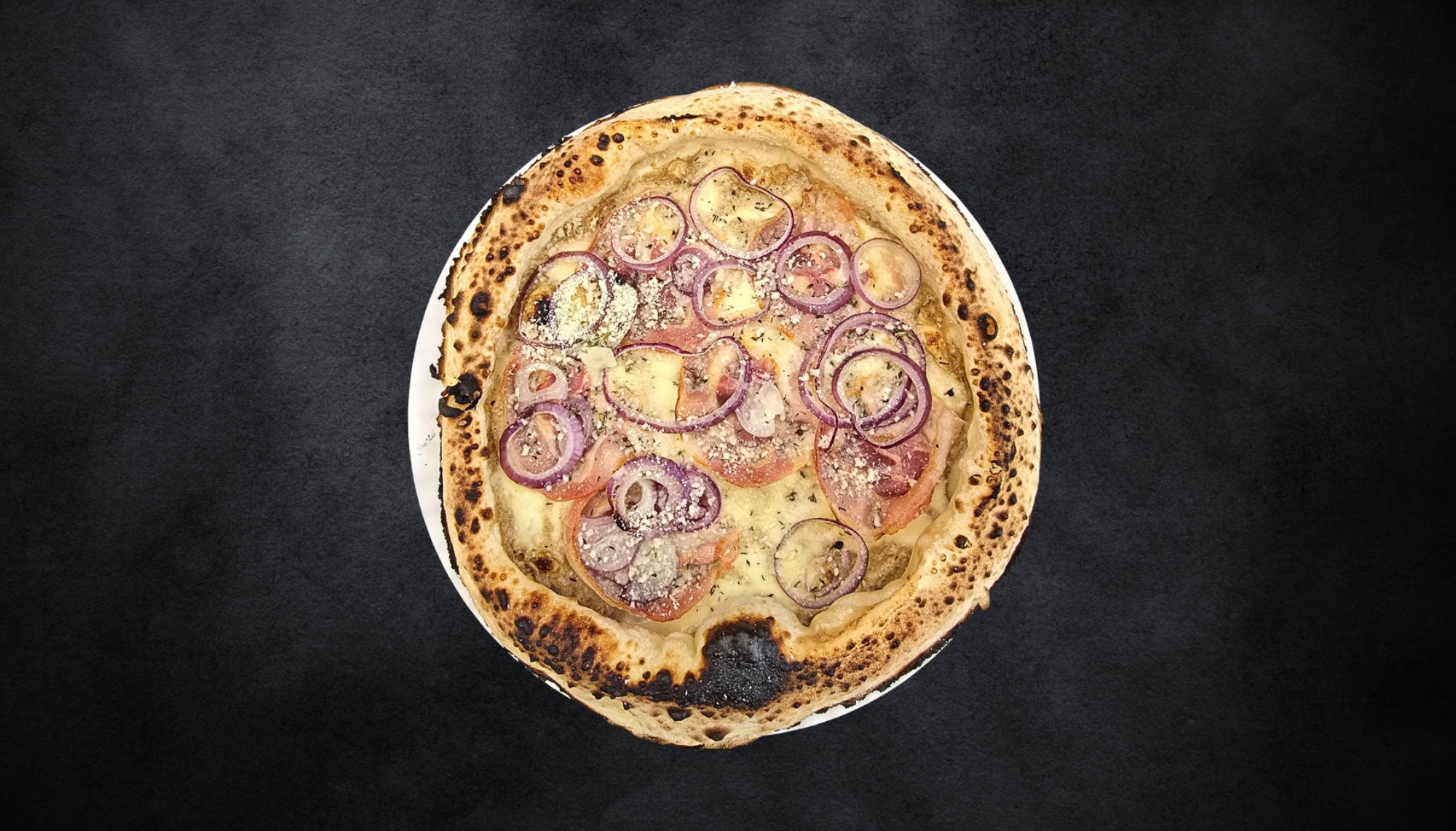 Pizza z serem, pomidorami i czerwoną cebulą na ciemnym tle.