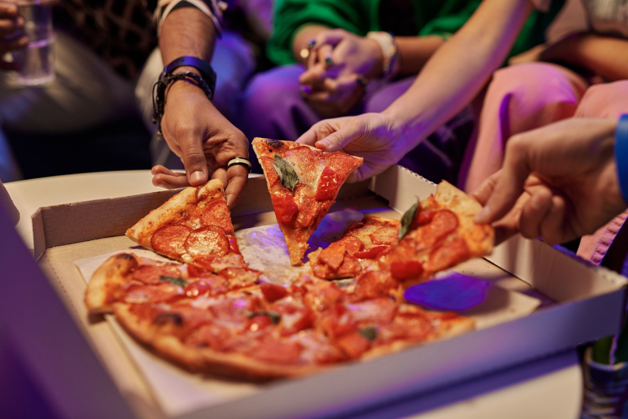Osoby dzielące się kawałkami pizzy w kartonowym pudełku na imprezie.