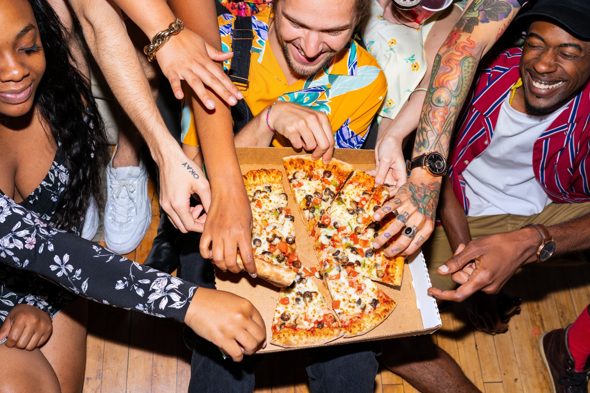 Grupa ludzi dzieląca się pizzą, z rękami sięgającymi po kawałki w radosnej atmosferze.