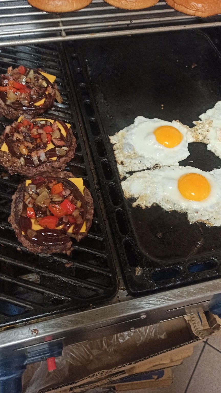 Burgerki z mięsem, serem i warzywami obok smażonych jajek na patelni.