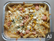 Makaron penne z łososiem, kukurydzą i serem, zapieczony z serem na wierzchu w metalowej formie.