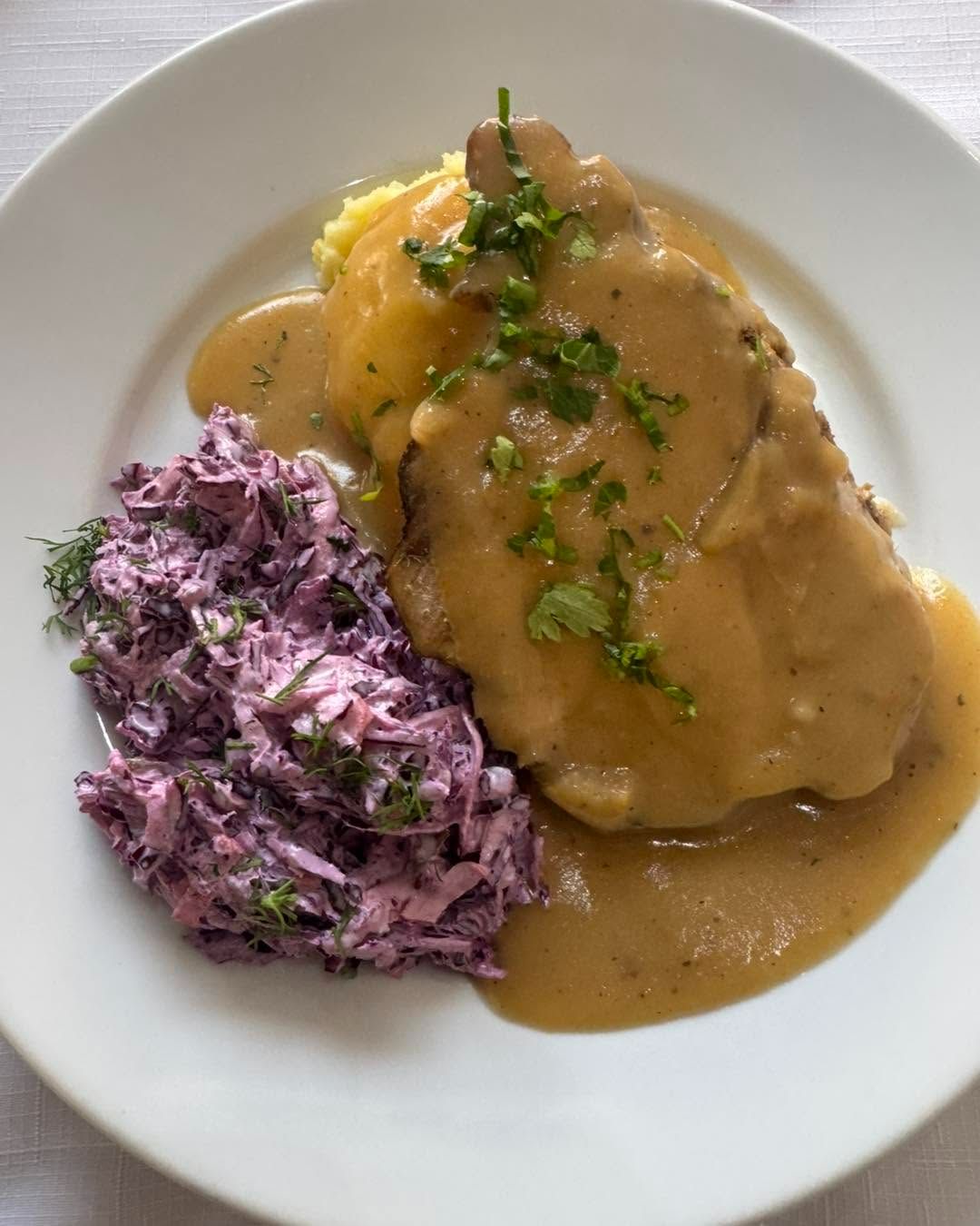 Obiad z mięsem w sosie, puree ziemniaczanym i sałatką z czerwonej kapusty posypaną ziołami.