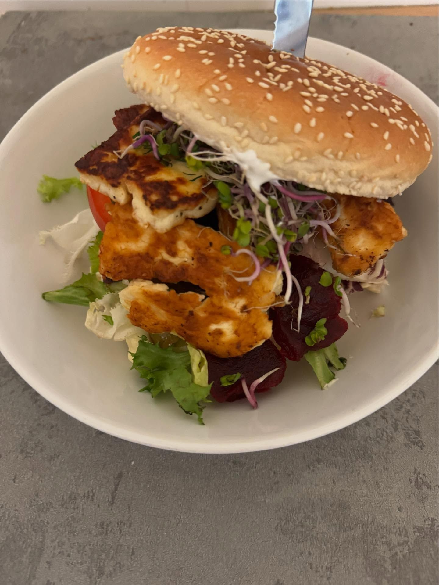 Burgery z serem halloumi, świeżą sałatą, pomidorem i kiełkami w bułce sezamowej.