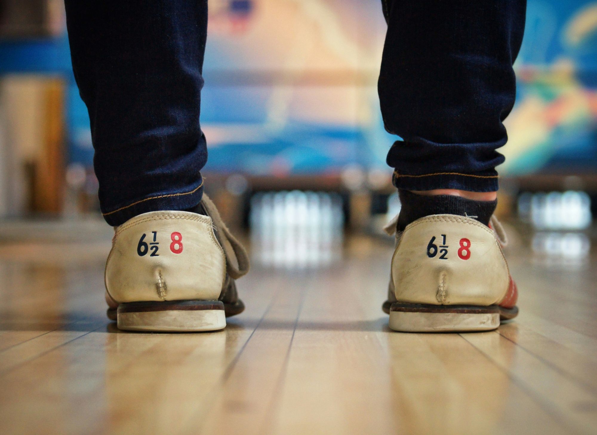 Osoby w specyficznych butach do bowlingu stojące na torze bowlingowym.