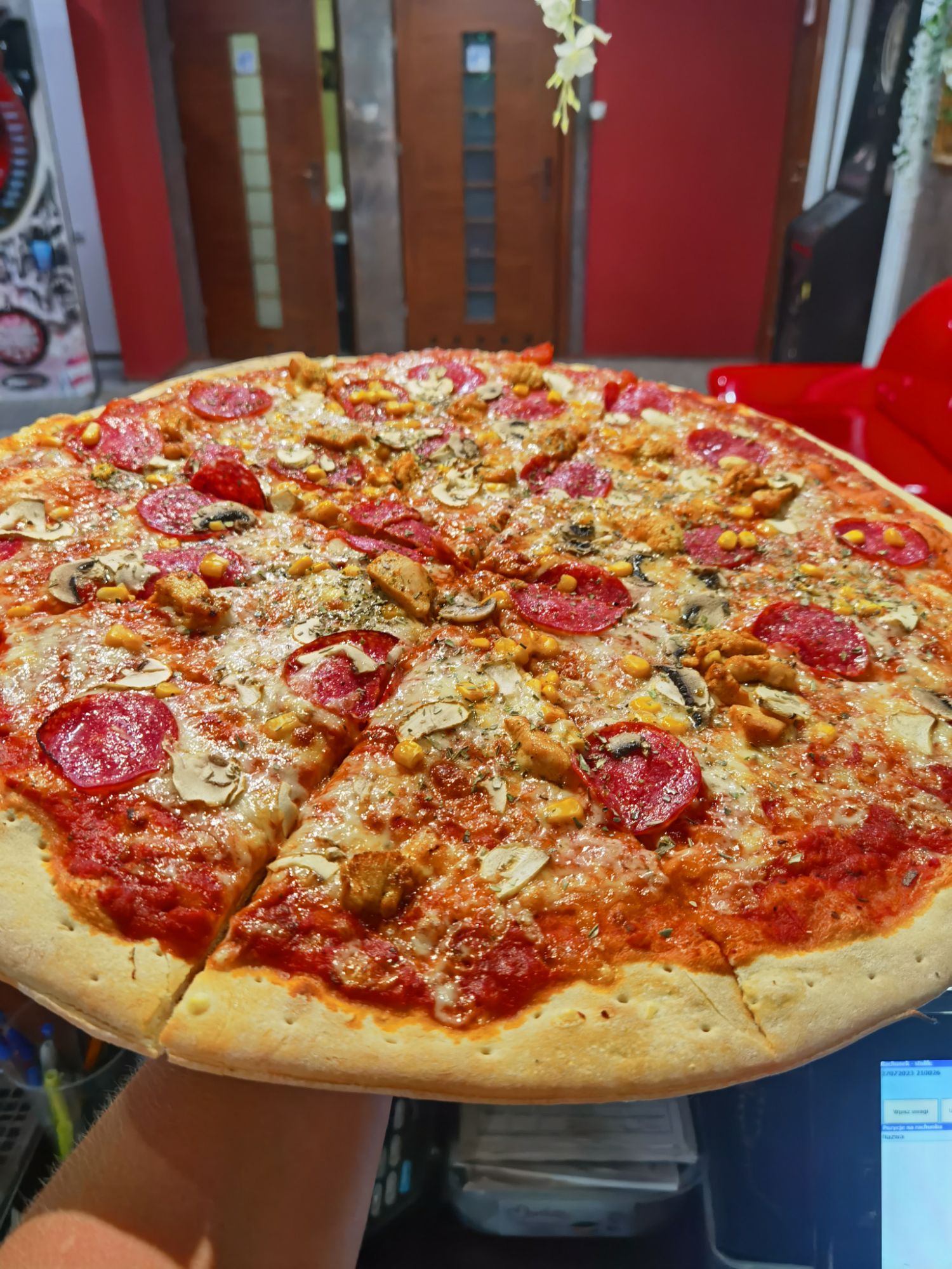 Pizza z pepperoni, serem i grzybami, trzymana w ręku na tle restauracji.