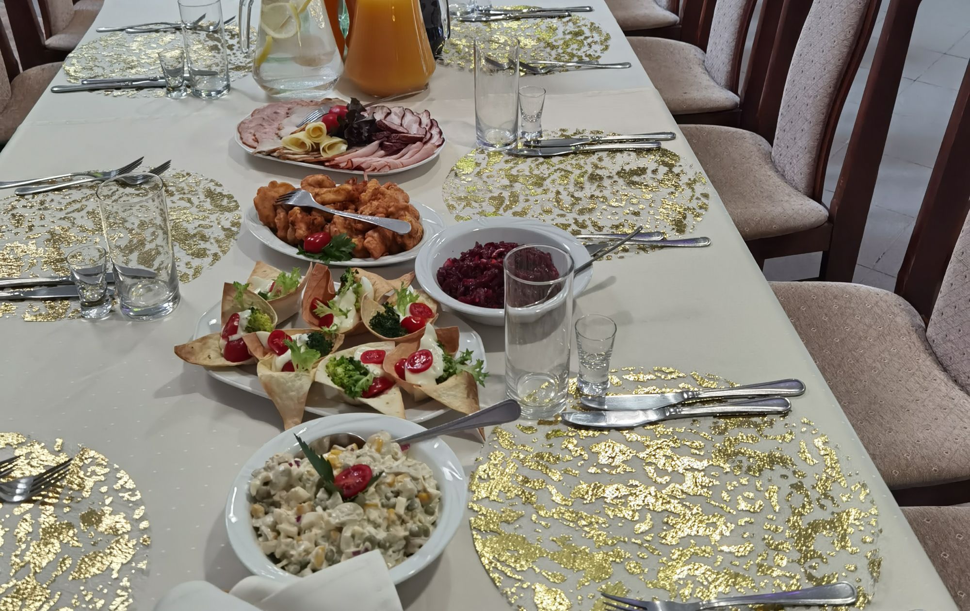 Stół z potrawami: sałatki, dania mięsne i napoje w eleganckim otoczeniu.