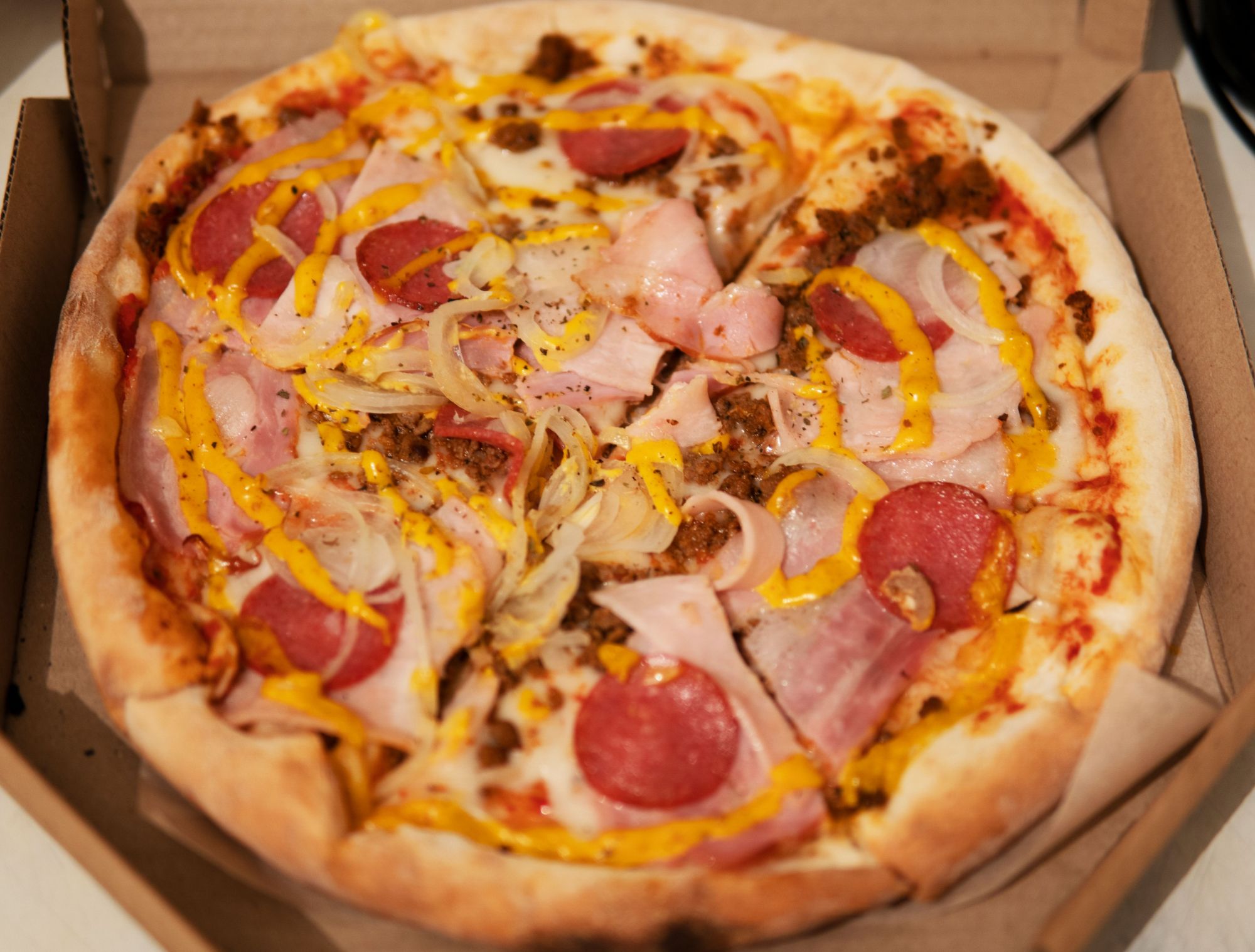 Pizza z serem, szynką, pepperoni, cebulą i ketchupem w opakowaniu.