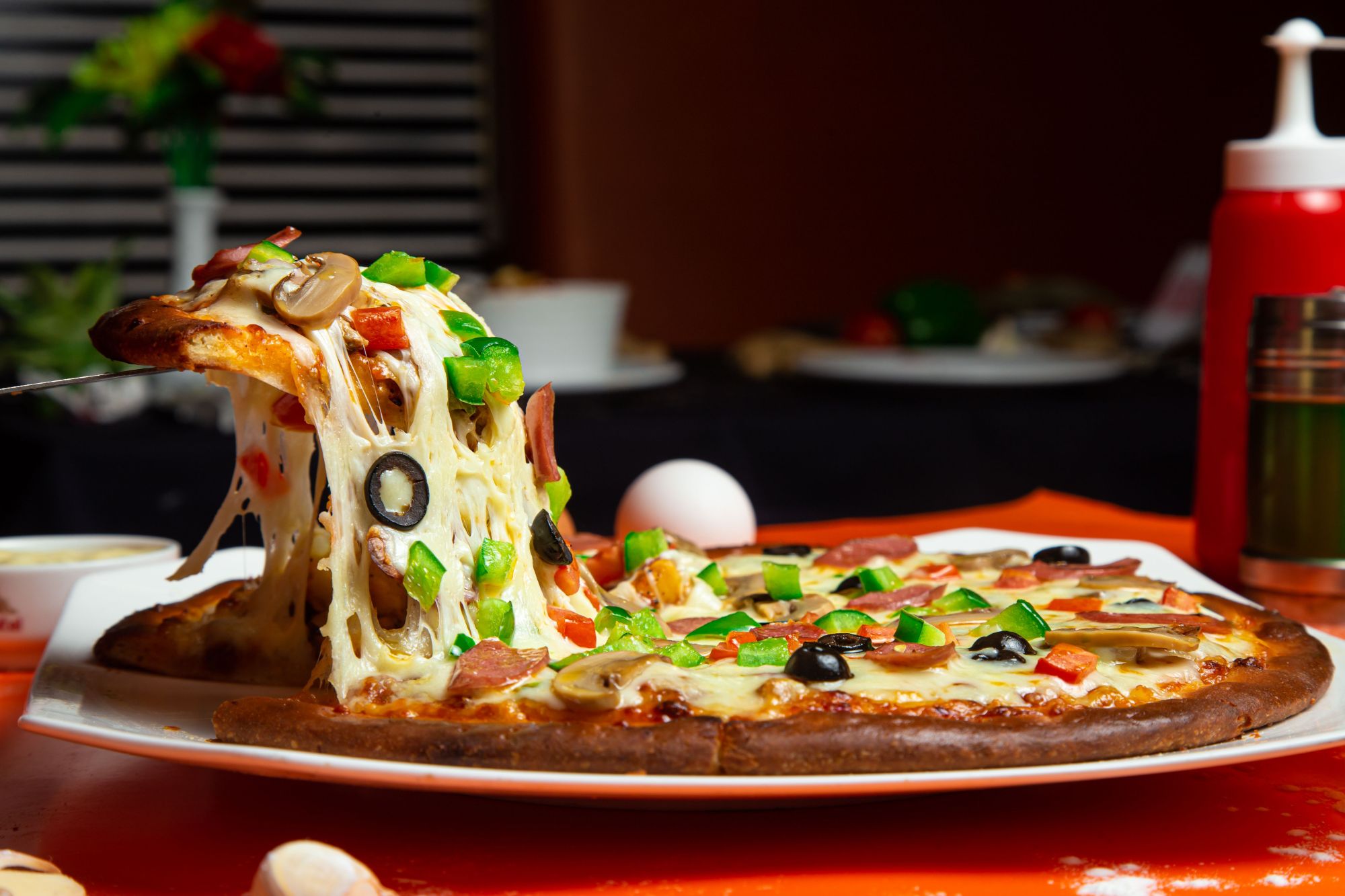 Pyszna pizza z serem, pieczarkami, oliwkami, papryką i boczkiem na talerzu w restauracji.