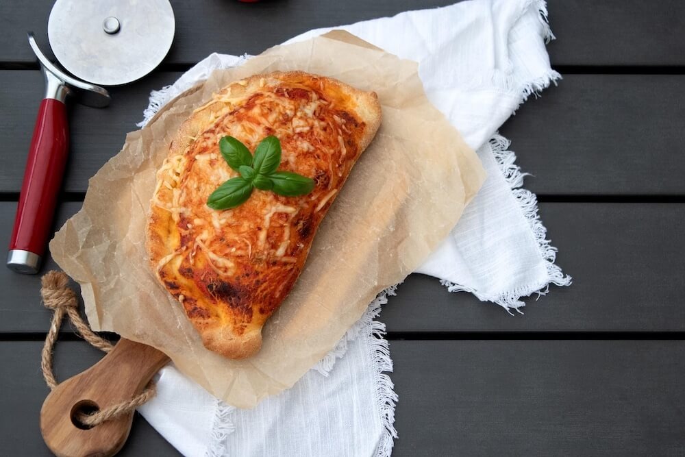 Calzone na papierze do pieczenia, leżące na drewnianej desce