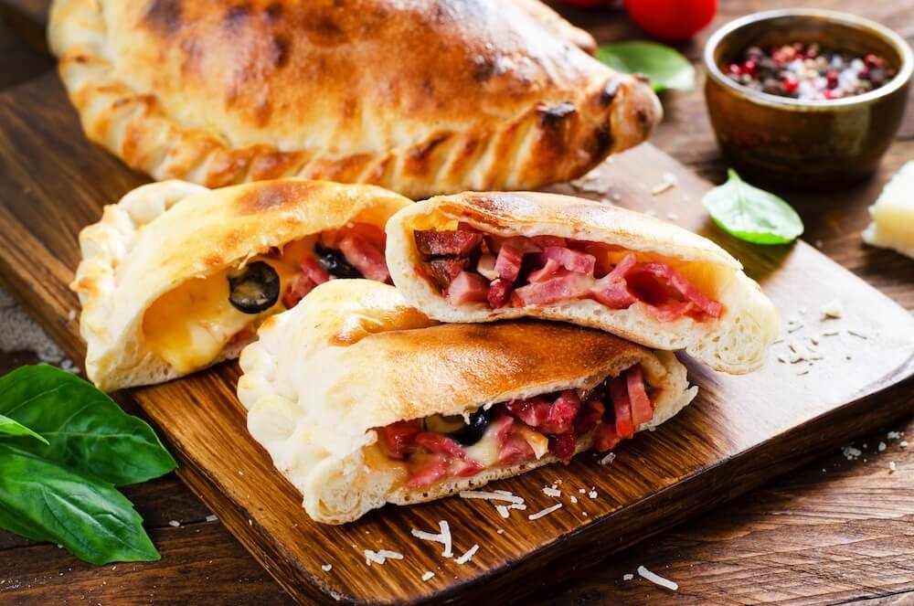 Pyszna pizza Calzone, tradycyjna włoska pizza nadziewana szynką i serem z pomidorami i świeżą bazylią na drewnianym tle