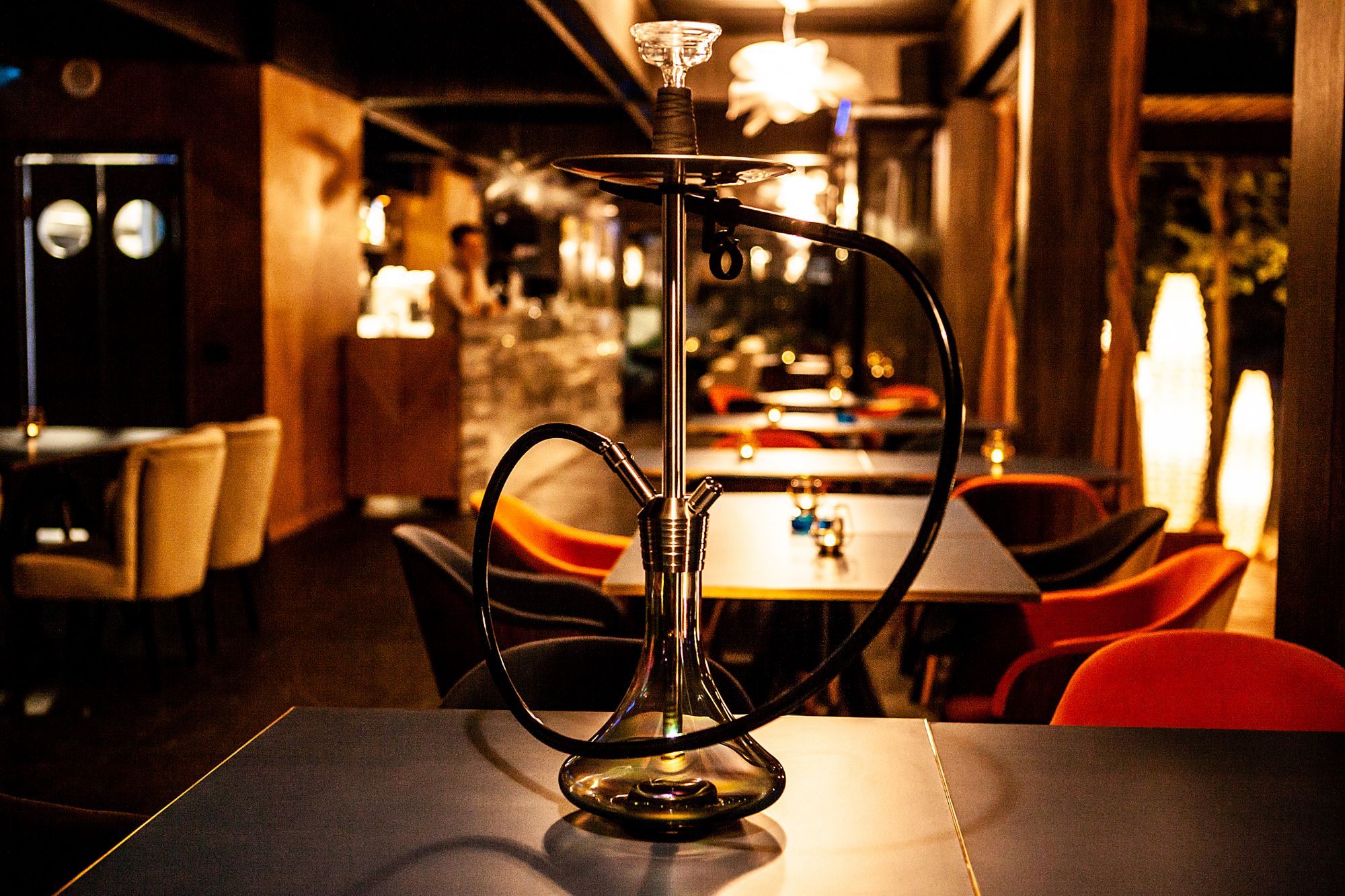 Szklana fajka wodna na stole w eleganckiej restauracji, w tle widoczne nowoczesne meble i oświetlenie.