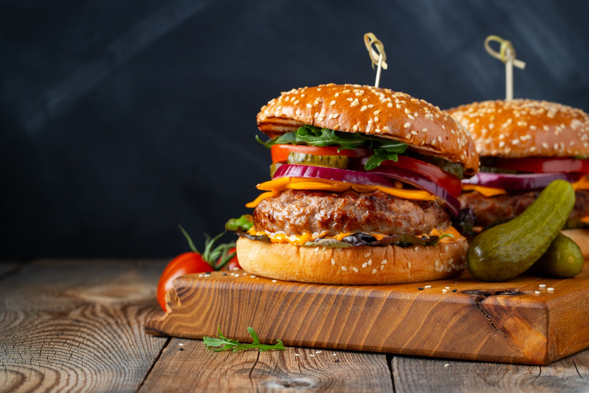 Soczysty burger z serem, świeżymi warzywami i ogórkiem na desce drewnianej.